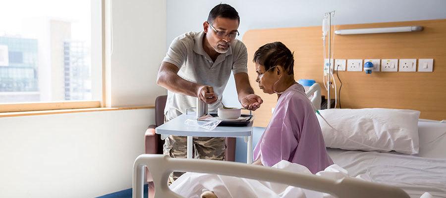 A man feeding his wife who is hospitalized with the flu