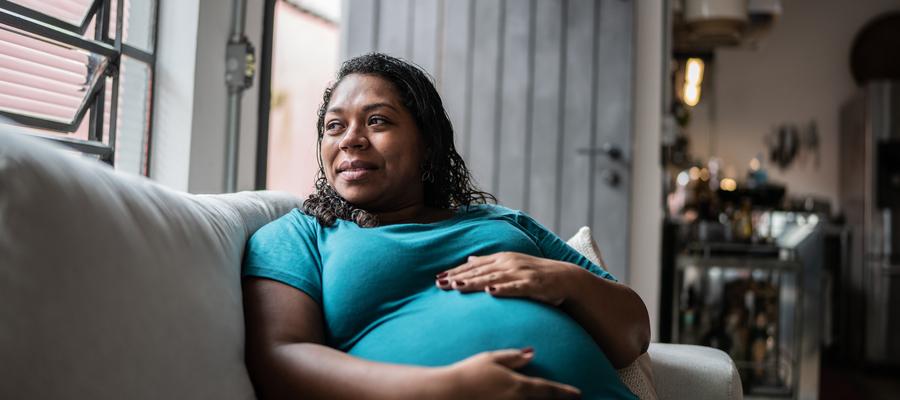 A pregnant woman holds her belly and looks out a window.