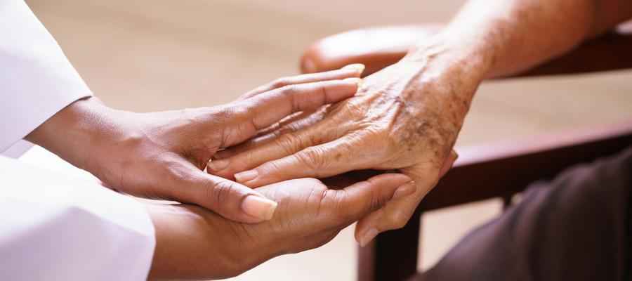 A health care worker gently holds the hand of an older patient.